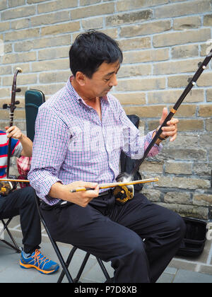 Beijing, China - September 2017: Chinese man playing the Chinese violin called erhu in a small ensemble outdoor at the temple of Heaven Stock Photo