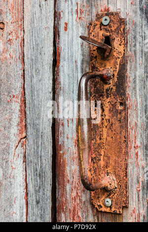 Close-up of rusted metal handle on old wooden grey and red painted barn door, background image Stock Photo