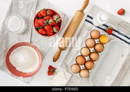 Raw ingredients for cooking strawberry pie or cake on white background  (eggs, flour, milk, sugar, strawberry), top view, flat lay. Bakery background. Stock Photo