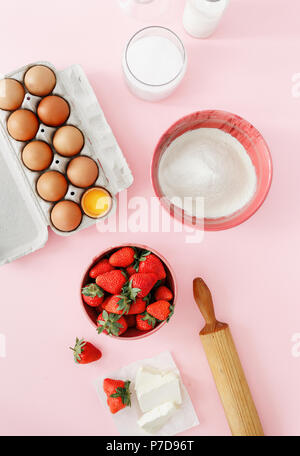 Raw ingredients for cooking strawberry pie or cake on pink background  (eggs, flour, milk, sugar, strawberry), top view, flat lay. Bakery background.  Stock Photo