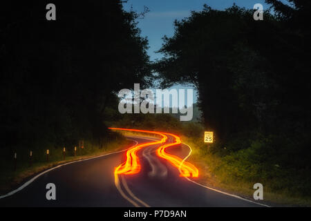 Car tail light trails on a winding road at night in forest. Stock Photo