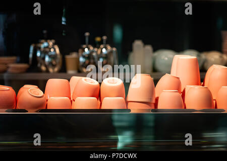 Upside-down pile of coffee cups of brown color behind the glass of an empty cafe. Stock Photo