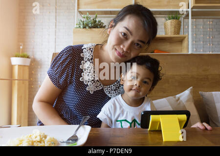 An Asian mother and 2 year old Asian boy, sitting on a table, smiling happily after breakfast at a restaurant. Stock Photo
