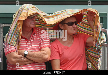 Spectators on court 17 shield themselves from the sun on day four of the Wimbledon Championships at the All England Lawn Tennis and Croquet Club, Wimbledon. Stock Photo