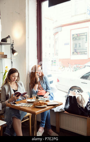 Women reading and chatting on mobile phone in cafe Stock Photo