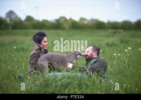 Man and woman reclining in field playing with dog Stock Photo