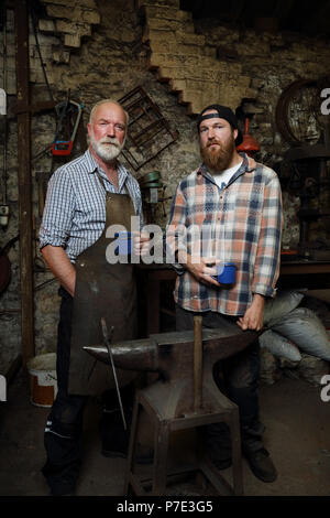 Senior blacksmith and son taking a break in blacksmiths shop, portrait Stock Photo