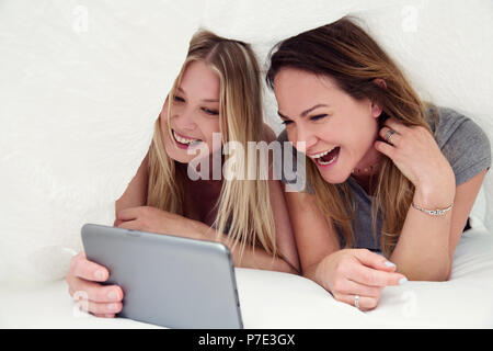 Friends underneath bed sheet using digital tablet smiling Stock Photo