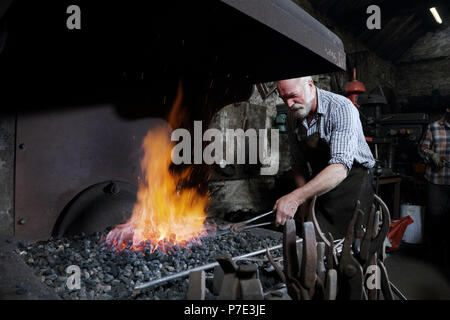 Blacksmith heating metal in forge fire in blacksmiths shop Stock Photo