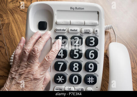 Visually impaired elderly woman dialling NHS 111 help line on big button telephone. Stock Photo