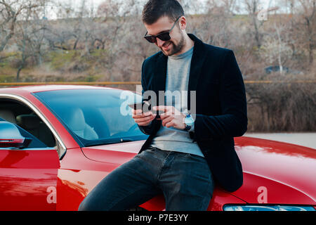 Portrait of man leaning against car texting on mobile phone Stock Photo