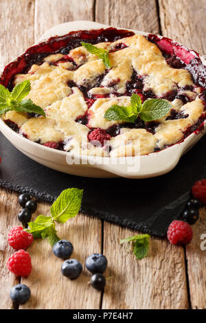 Delicious dessert: a sweet cobbler of raspberries, currants and blueberries close-up in a baking dish on a table. vertical Stock Photo