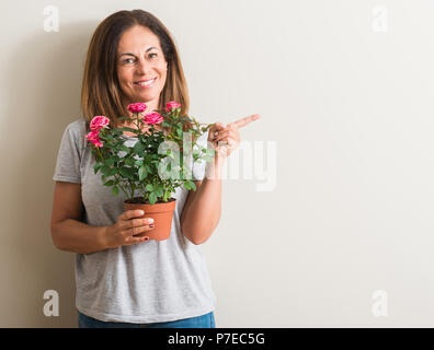 Middle age woman holding roses flowers on pot pointing with hand and finger  up with happy face smiling Stock Photo