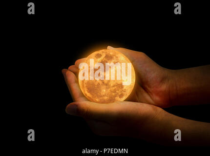 Female hand hold yellow full moon on her hand. A full moon is the lunar phase that occurs when the Moon is completely illuminated as seen from Earth. Stock Photo