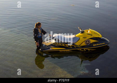 29 June 2018 A young woman in a wet suit waits for her partner beside a powerful Yamaha Jet-Ski on the slipway  at Groomsport Harbour Northern Ireland Stock Photo