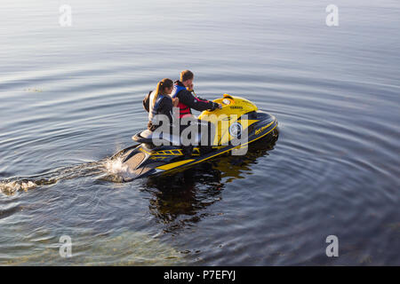 29 June 2018 A young couple on board a powerful Yamaha Jet-Ski as they head to sea from Groomsport Harbour Northern Ireland on a flat calm evening Stock Photo