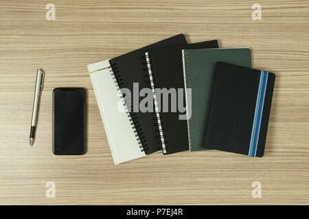 Messy stack of books on wood background with smartphone and pen on wood background. Stock Photo