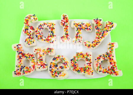 Fairy bread spelled with fairy bread on a white rectangular plate on bright green background. Fairy bread is commonly served at children's parties in  Stock Photo