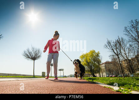 Young pretty girl running outdoor in the spring with her Bernese Mountain dog Stock Photo