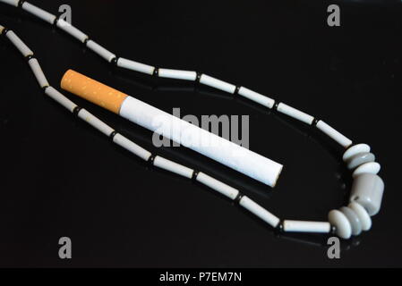 One cigarette and gray female beads on a black glossy background. Stock Photo