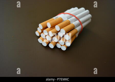 Cigarettes from the pack are fixed with a red rubber band on a brown matte background. Stock Photo