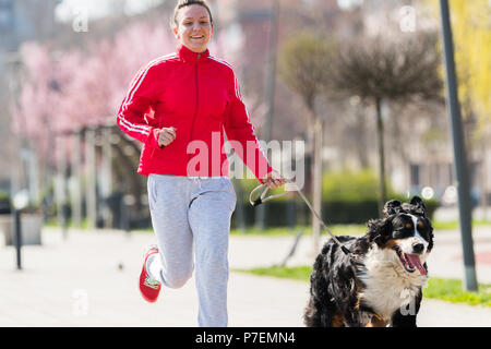 Young pretty girl running outdoor in the spring with her Bernese Mountain dog Stock Photo