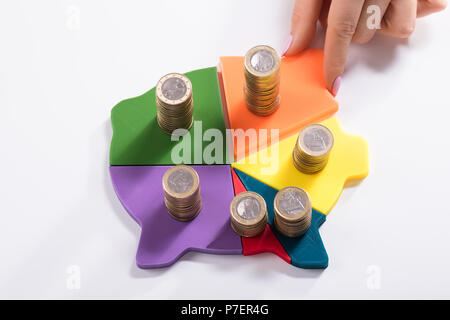 Woman's Hand Placing Last Piece Into Multi Colored Piggybank With Stacked Coins On White Background Stock Photo