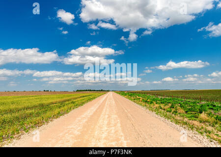 White, puffy clouds moving over remote dirt road and flat lands in the Great Plains, Oklahoma. Stock Photo