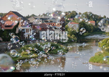 Magical, unreal, dreamy landscape with soap bubbles curtain in air over river and town with houses, buildings Stock Photo