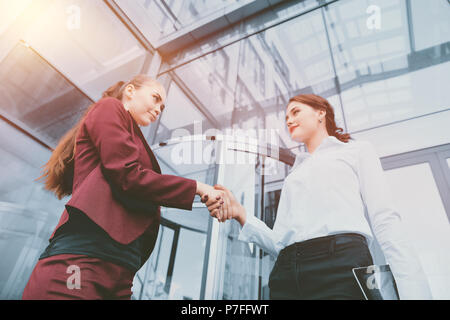 Handshake of two young girls against the background of a multi-storey office building. Make a deal. Friendly relations. Office staff. Stock Photo