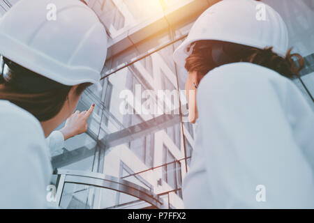 Girls in building white helmets with tablets in hands on the background of a glass office building. Women are engineers. Female professions. Stock Photo
