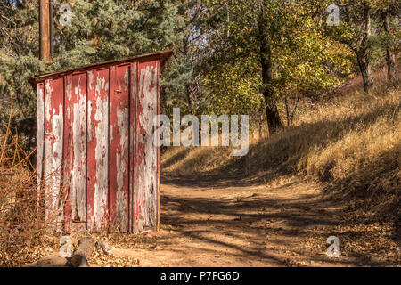 Old, peeling red paint on small, wood vintage out building on rural path in the autumn Stock Photo