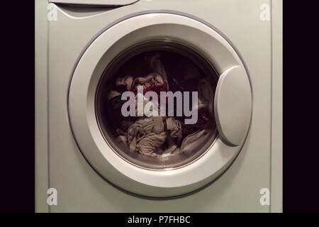 A close up of a washing machine loaded with clothes isolated on white background. The Laundry in the washing machine with the closed open. Stock Photo