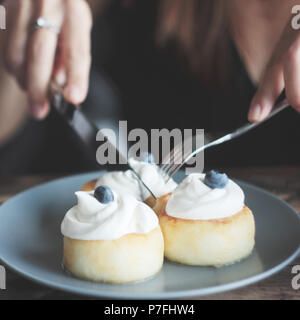 Cheesecakes with cream and blueberries on blue plate, women's hands with knife and fork Stock Photo