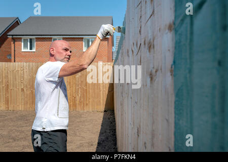 Man using a paintbrush to paint a garden fence green Stock Photo