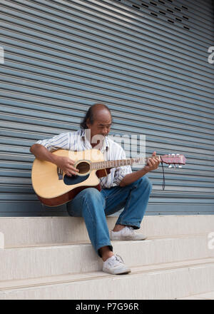 Senior man sitting on steps and playing guitar, Vientiane, Laos, Asia. Stock Photo