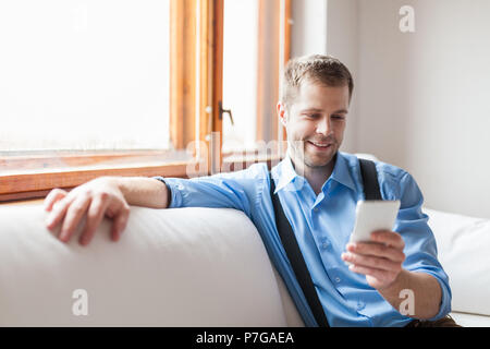 Handsome man sitting on sofa and texting from his smart phone Stock Photo