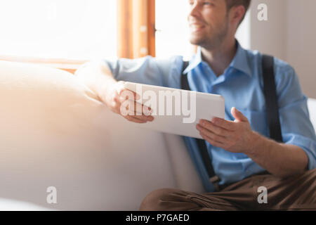 Handsome man sitting on sofa at home, using a digital tablet Stock Photo