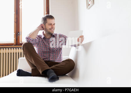 Handsome man sitting on sofa at home, using a digital tablet Stock Photo