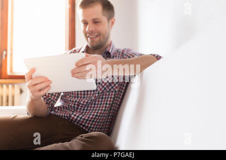 Handsome man sitting on sofa at home, using a digital tablet Stock Photo