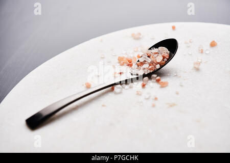 Black spoon of pink himalayan salt on marble cutting board with copy space. Stock Photo