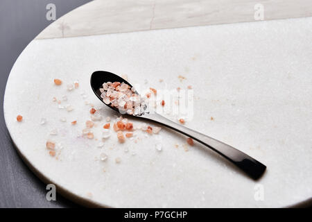 Black spoon of pink himalayan salt on marble cutting board with copy space. Stock Photo