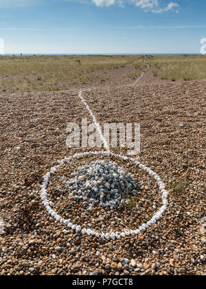 Small stone and shell cairn on a shingle beach in a ring of white sea shells and a line running from it down to the sea, Shingle Street,Suffolk Stock Photo