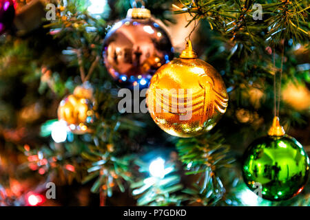 Closeup of hanging illuminated orange, green, blue, colorful, multicolored, multi-colored Christmas ornament on pine tree with lights Stock Photo