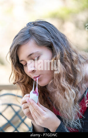 One young woman on chair, holding, eating piece of homemade mochi sticky glutinous Japanese rice cake dessert outdoors, sitting outside on deck Stock Photo