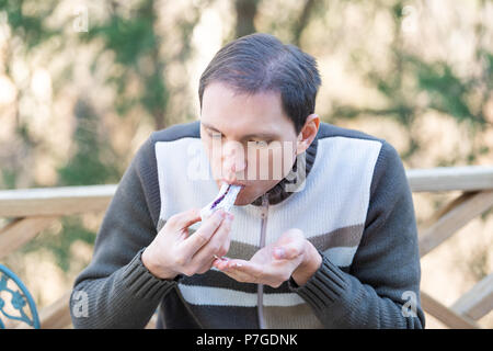 One young man sitting on chair, holding, eating piece of homemade mochi sticky glutinous Japanese rice cake dessert outdoors, outside on deck Stock Photo