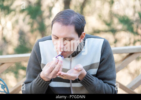 Young man sitting on chair, holding, eating one piece of homemade mochi sticky glutinous Japanese rice cake dessert outdoors, outside on deck Stock Photo