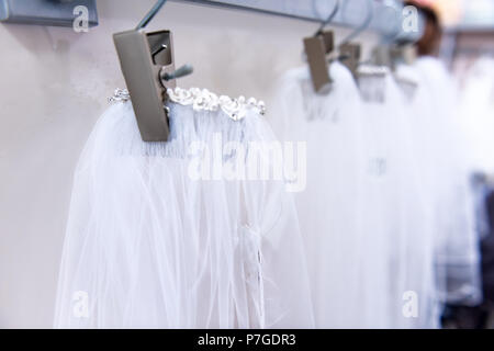 Many wedding veils in boutique discount store, white garments hanging on rack hangers row closeup with white lace, tulle, design Stock Photo
