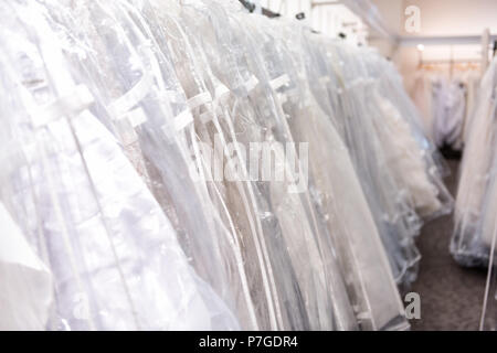 Many wedding dresses in boutique discount store, white garments hanging on rack hangers row closeup with white lace, tulle, design Stock Photo