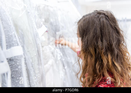 One woman searching, trying on, choosing, touching wedding dresses in boutique discount store, many white garments hanging on rack hangers in row Stock Photo